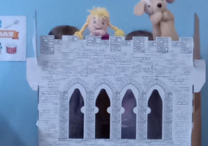 Dwoje dzieci schowanych za makieta zamku animuje pacynki psa i dziewczynki.